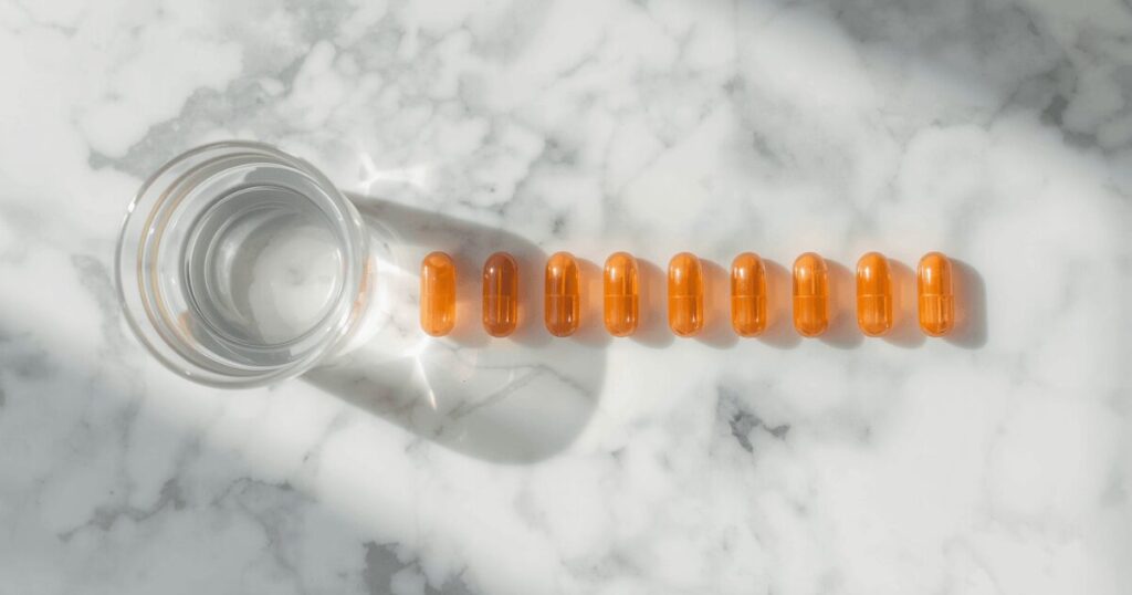 サプリメントのカプセルと水のグラスが並んでいる、清潔感のある白い背景の写真