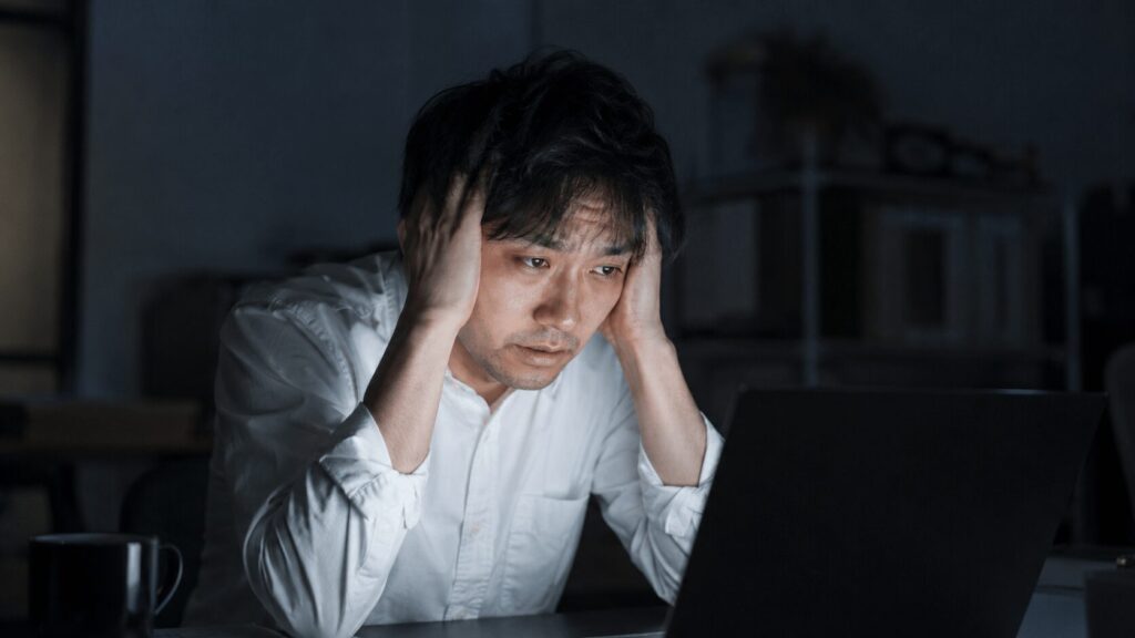 デスクで疲れた様子の男性と不健康な生活習慣を象徴するイメージ