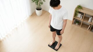 体組成計に乗って体脂肪率を測定する男性