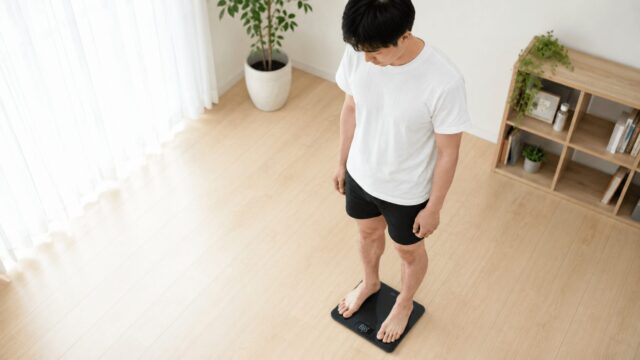 体組成計に乗って体脂肪率を測定する男性
