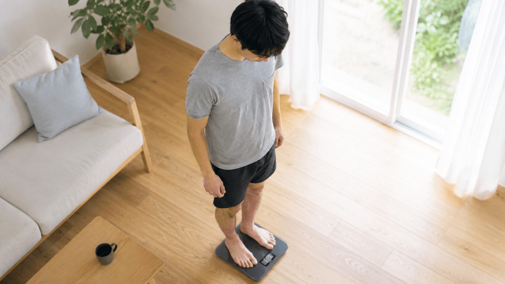 自宅で体組成計に乗って体脂肪率を測定する男性