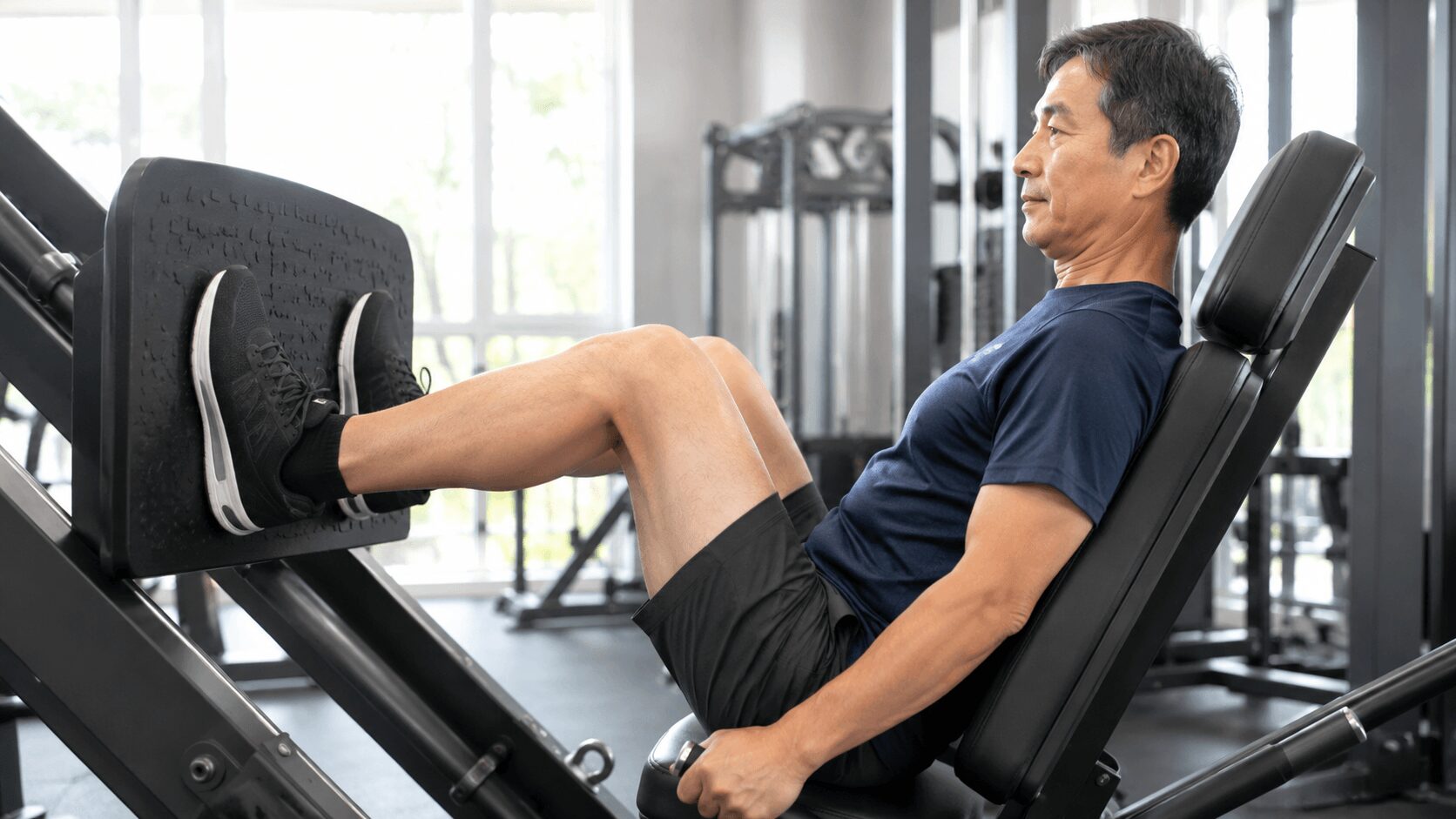 ジムのレッグプレスマシンで脚を鍛える50代男性