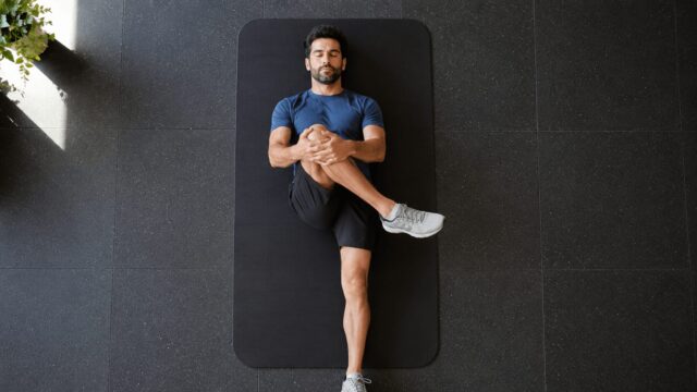 ジムのフロアで筋トレ前のウォームアップストレッチを行う男性の俯瞰イメージ