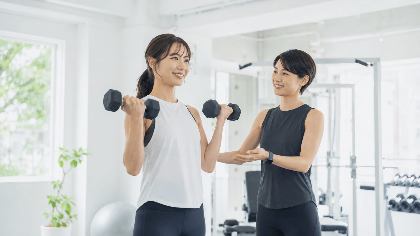 女性専用パーソナルジムでトレーナーの指導を受けながらトレーニングする女性