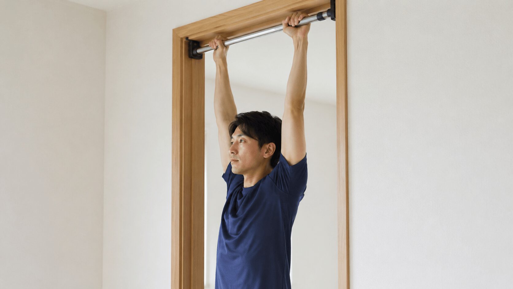 自宅のドア枠に取り付けた懸垂バーにぶら下がる男性