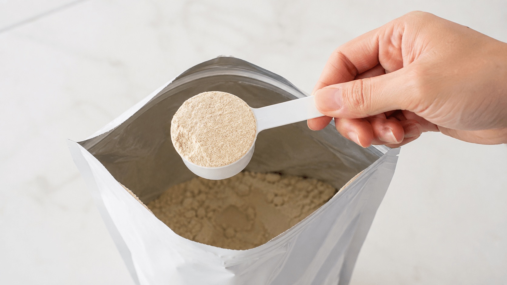 プロテインの付属スプーンで粉を計量し1食あたりの量を確認する手元