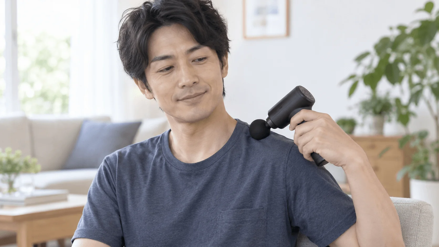 首を避けて肩の付け根にマッサージガンを弱く当てる男性
