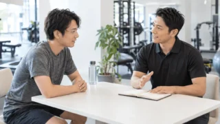 筋トレを管理してもらうためにトレーナーと相談する男性